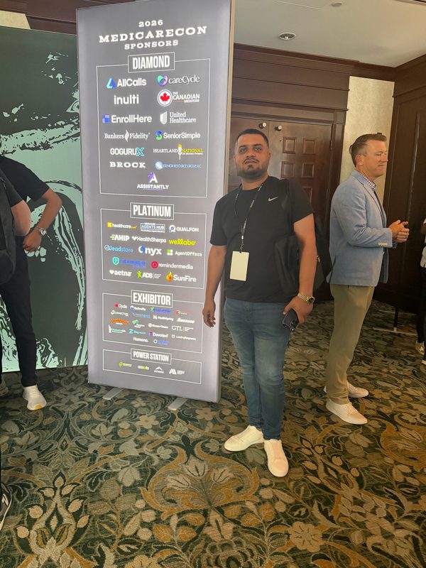 Wali Zuberi standing beside a MedicareCon 2026 event banner in the conference hallway